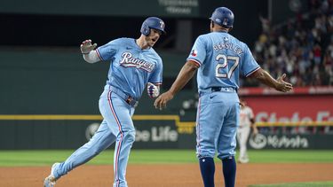 Jonah Heim, izquierda, de los Rangers de Texas, es felicitado por el coach de tercera base Tony Beasley (27) mientras se enfila al plato con su cuadrangular de tres carreras en el que también anotaron Wyatt Langford y Nathaniel Lowe durante la cuarta entrada del juego de béisbol en contra de los Orioles de Baltimore, el domingo 21 de julio de 2024, en Arlington, Texas. (AP Foto/Jeffrey McWhorter)