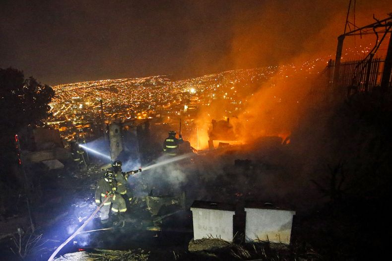Los bomberos rocían agua sobre casas en llamas durante un incendio forestal en Valparaíso, Chile, el miércoles 13 de marzo de 2024 por la noche. (Sebastián Cisternas, Aton Chile vía AP)