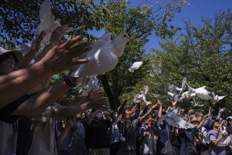 Visitantes liberan palomas blancas en el Santuario Yasukuni en el 80mo aniversario de la rendición de Japón en la Segunda Guerra Mundial, en Tokio, el viernes 15 de agosto de 2025. (AP Foto/Louise Delmotte)