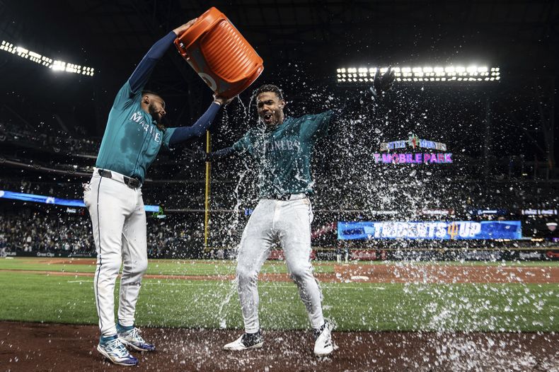 J.P. Crawford, de los Marineros de Seattle, vacía la hielera encima del dominicano Julio Rodríguez, quien conectó el batazo decisivo ante los Medias Rojas de Boston, el sábado 30 de marzo de 2024 (AP Foto/Stephen Brashear)