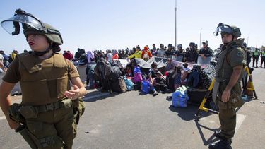 Carabineros al lado de migrantes sentados en una carretera cerca de Arica, Chile, el jueves 27 de abril de 2023. Una crisis migratoria en la frontera entre Chile y Perú se intensificó con la llegada de cientos de personas que quedaron varadas, al no poder cruzar a Perú desde Chile en su ruta para regresar a sus países de origen. (Patricio Banda/Aton Chile vía AP)
