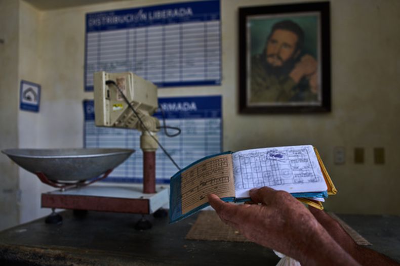 Un hombre muestra su cartilla de racionamiento, conocida como libreta, mientras al fondo se ve una imagen enmarcada de Fidel Castro, en una bodega estatal en La Habana, Cuba, el sábado 2 de mayo de 2026. (AP Foto/Ramón Espinosa)