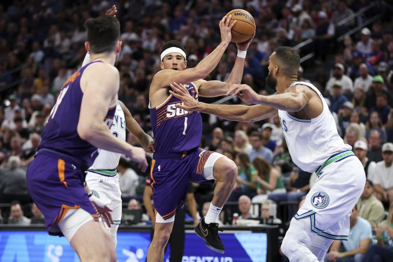 El escolta de los Suns de Phoenix, Devin Booker (1), avanza hacia la canasta mientras el pívot de los Timberwolves de Minnesota, Rudy Gobert, a la derecha, defiende durante la segunda mitad del partido de baloncesto de la NBA, el domingo 14 de abril de 2024, en Minneapolis. (AP Foto/Matt Krohn)
