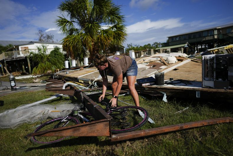 Jessica Long trata de sacar la bicicleta de su sobrina de debajo de un trozo de la vivienda vacacional de la familia, que quedó destrozada por la marejada ciclónica causada por Idalia, en Horseshoe Beach, Florida, el 31 de agosto de 2023, un día después del paso del huracán. (AP Foto/Rebecca Blackwell)