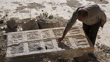 Un guardia inspecciona una piedra tallada, hallada originalmente en un complejo de tumbas subterráneas bizantinas que se cree tienen más de 1.500 años de antigüedad y fueron reveladas por un contratista durante la reconstrucción de una casa destruida en un ataque y que ahora se encuentra en el patio de un museo en Maarat al-Numan, Siria, el viernes 30 de mayo de 2025. (AP Foto/Omar Albam)