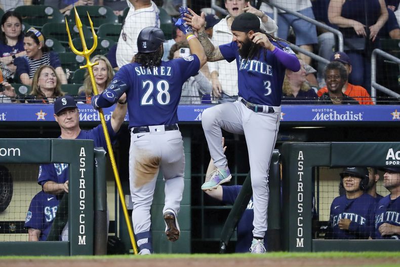 El venezolano Eugenio Suárez de los Marineros de Seattle sostiene un tridente mientras celebra con J.P. Crawford su segundo jonrón de la noche en la novena entrada ante los Astros de Houston el jueves 6 de julio del 2023. (AP Foto/Michael Wyke)