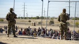 Migrantes esperan junto a una valla fronteriza mientras son vigilados por miembros de la Guardia Nacional de Texas, para ingresar a El Paso, Texas, el miércoles 10 de mayo de 2023. (AP Foto/Andres Leighton)