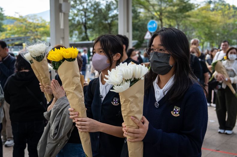 Gente lleva flores para las víctimas cerca del lugar de un incendio mortal iniciado el miércoles en Wang Fuk Court, un complejo residencial en el distrito Tai Po de los Nuevos Territorios de Hong Kong, el lunes 1 de diciembre de 2025. (AP Foto/Chan Long Hei)