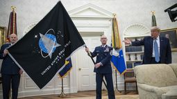 El general John Jay Raymond, comandante del Comando Espacial Estadounidense (izq) y el sargento Roger Towberman (der) sostienen la bandera al lado del presidente Donald Trump durante la presentación de la bandera del Comando Espacial en la Oficina Oval en la Casa Blanca en Washington el 15 de mayo del 2020. (AP foto/Alex Brandon)