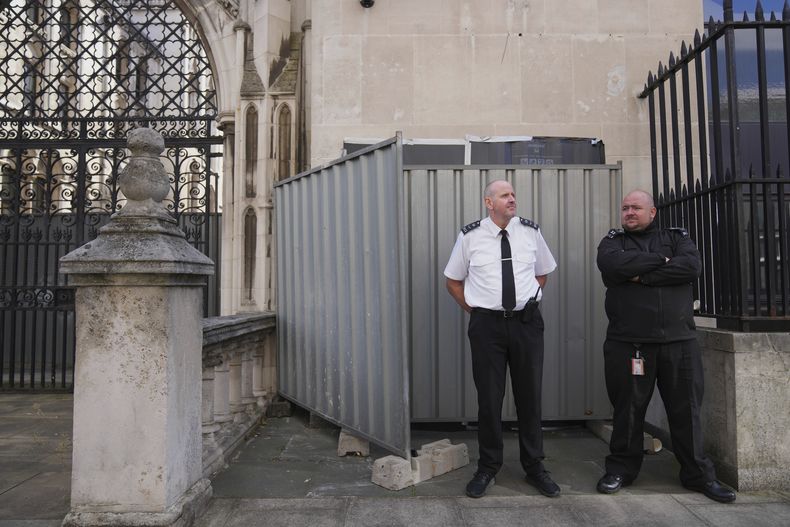 Guardias frente a láminas de plástico negro y dos barreras de metal que ocultan la más reciente obra de arte del artista callejero Banksy, en la que un manifestante yace en el suelo sosteniendo una pancarta salpicada de sangre mientras un juez con una peluca tradicional y una toga negra lo golpea con un mazo, afuera de los Tribunales Reales de Justicia en Londres, el lunes 8 de septiembre de 2025. (Foto AP/Joanna Chan)