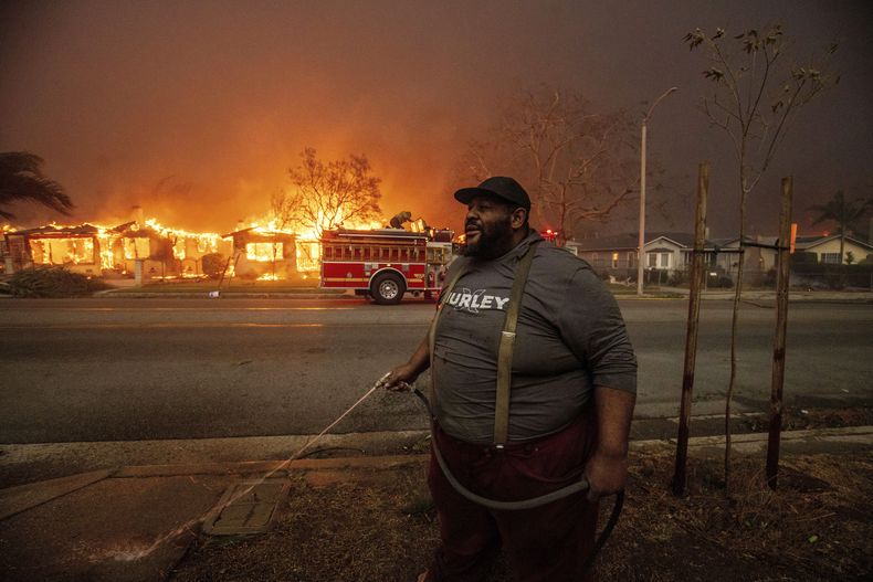 ARCHIVO - Un vecino arroja agua a su propiedad con una manguera de jardín mientras el incendio Eaton arrasa las estructuras situadas al otro lado de la calle, el miércoles 8 de enero de 2025 en Altadena, California. (AP foto/Ethan Swope, archivo)