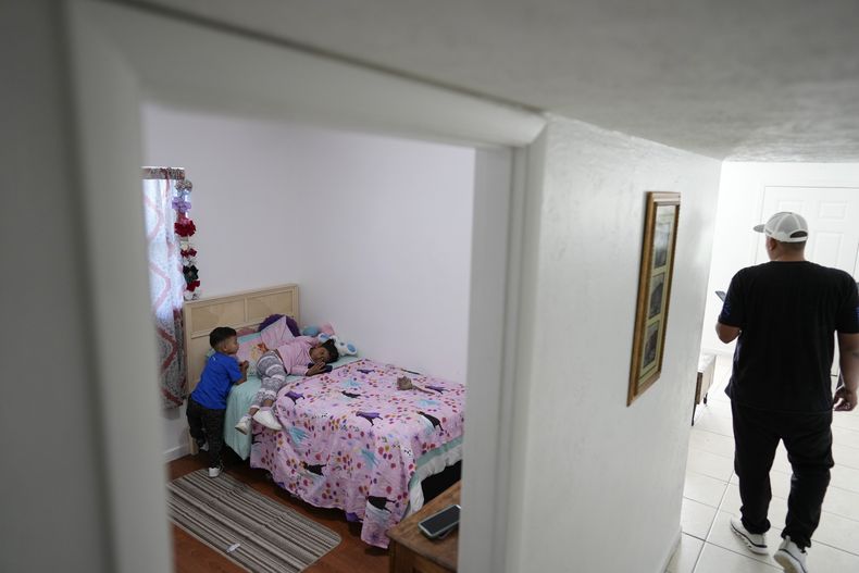 Alexis Llanos, a la derecha, se aleja después de haber permanecido en el cuarto de sus hijos Alexa, de 7 años, y Alexis, de 3, en la casa de Lehigh Acres, en Florida, a la que se mudaron en octubre de 2023, cinco años después de haber salido de Venezuela hacia Colombia por amenazas de muerte, el 27 de diciembre de 2023. La de Llanos es una de las primeras familias de migrantes que llegaron a Estados Unidos legalmente bajo un nuevo programa conocido como Oficinas de Movilidad Segura, que busca agilizar el proceso de refugiados. (AP Foto/Rebecca Blackwell).