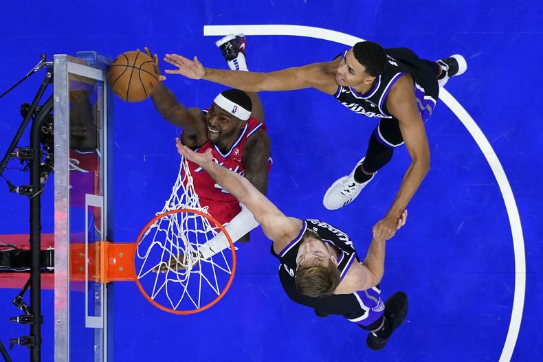 Paul Reed, izquierda, de los 76ers de Filadelfia, gana un rebote a Domantas Sabonis, abajo, y Keegan Murray, de los Kings de Sacramento, durante la primera mitad del juego de baloncesto de la NBA, el viernes 12 de enero de 2024, en Filadelfia. (AP Foto/Matt Slocum)