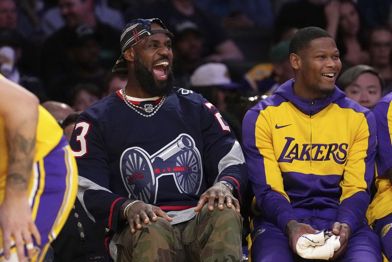 LeBron James, de los Lakers de Los Ángeles, a la izquierda, se ríe mientras se sienta en el banquillo durante la primera mitad de un partido de baloncesto de la NBA contra los Nuggets de Denver, el miércoles 19 de marzo de 2025, en Los Ángeles. (AP Foto/Mark J. Terrill)
