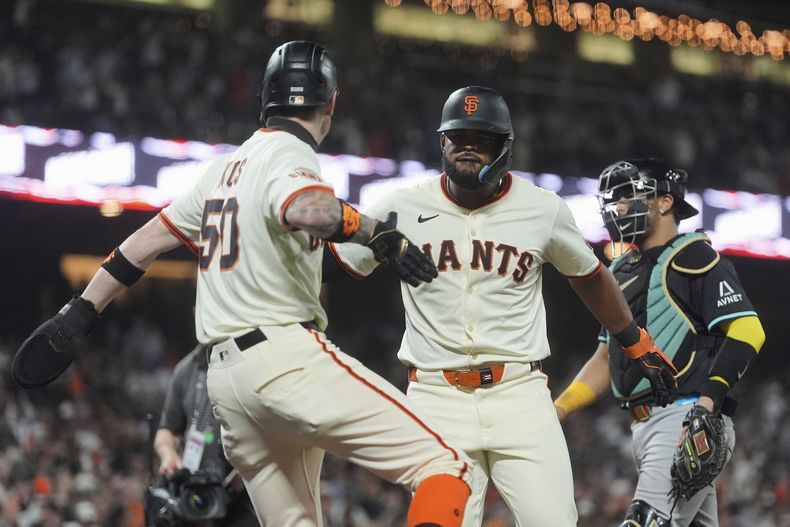 Heliot Ramos, centro, de los Gigantes de San Francisco, celebra después de batear un cuadrangular de dos carreras que remolcó a Christian Koss, izquierda, mientras el receptor de los Diamondbacks de Arizona, derecha, reacciona en la sexta entrada del juego de béisbol de Grandes Ligas, el lunes 8 de septiembre de 2025. (AP Foto/Jeff Chiu)