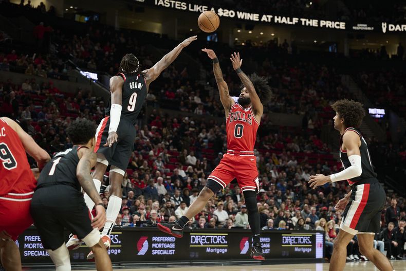 El base de los Bulls de Chicago Coby White lanza el balón sobre el alero de los Trail Blazers de Portland Jerami Grant en el encuentro de la NBA del domingo 28 de enero del 2024. (AP Foto/Troy Wayrynen)
