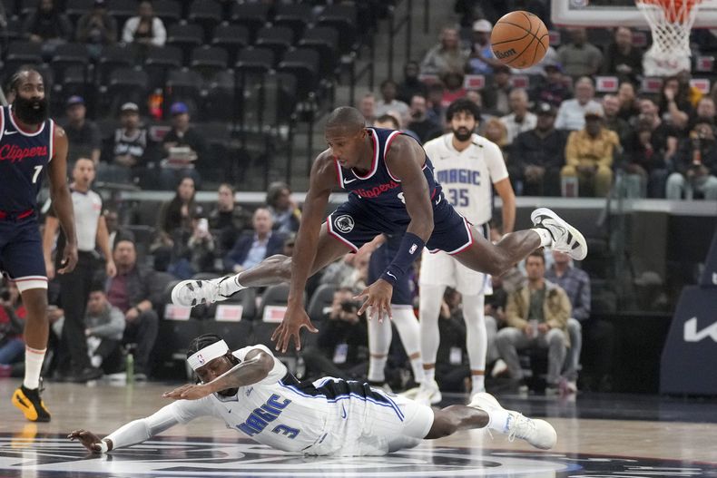 Kris Dunn, de los Clippers de Los Ángeles, y Kentavious Caldwell-Pope, del Magic de Orlando, disputan un balón perdido en el encuentro del miércoles 20 de noviembre de 2024 (AP Foto/Eric Thayer)