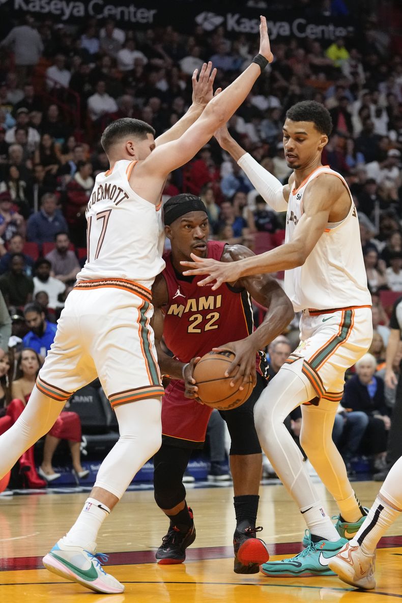 Jimmy Butler (22), del Heat de Miami, es presionado por dos torres de los Spurs de San Antonio, Doug McDermott (17) y Victor Wembanyama, durante la primera mitad del juego de baloncesto de la NBA, el miércoles 7 de febrero de 2024, en Miami. (AP Foto/Rebecca Blackwell)