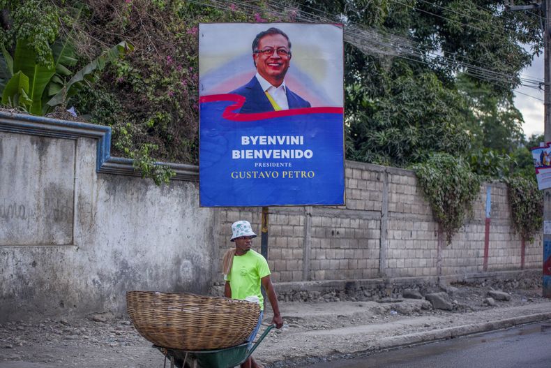 Un vendedor ambulante pasa frente a un cartel en el que se da la bienvenida al presidente de Colombia Gustavo Petro para una visita de un día, el miércoles 22 de enero de 2025, en Jacmel, Haití. (AP Foto/Patrice Noel)