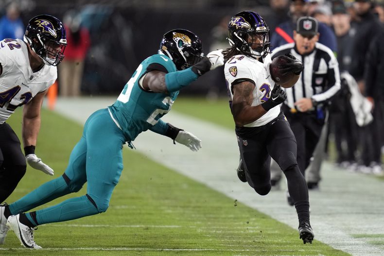 Keaton Mitchell (34), running back de los Ravens de Baltimore, intenta superar al linebacker Foyesade Oluokun (23), de los Jaguars de Jacksonville, en la primera mitad del juego de la NFL, el domingo 17 de diciembre de 2023, en Jacksonville, Florida. (AP Foto/John Raoux)