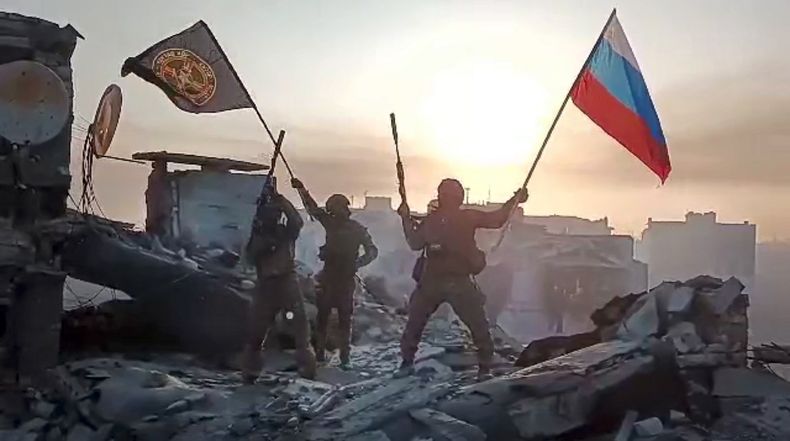 En esta imagen tomada de un video difundido por el Servicio de Prensa Prigozhin el sábado 20 de mayo de 2023, integrantes de la compañía militar Grupo Wagner de Yevgeny Prigozhin ondean una bandera rusa y otra del Grupo Wagner en una estructura dañada en Bájmut, Ucrania. (Servicio de Prensa Prigozhin vía AP)